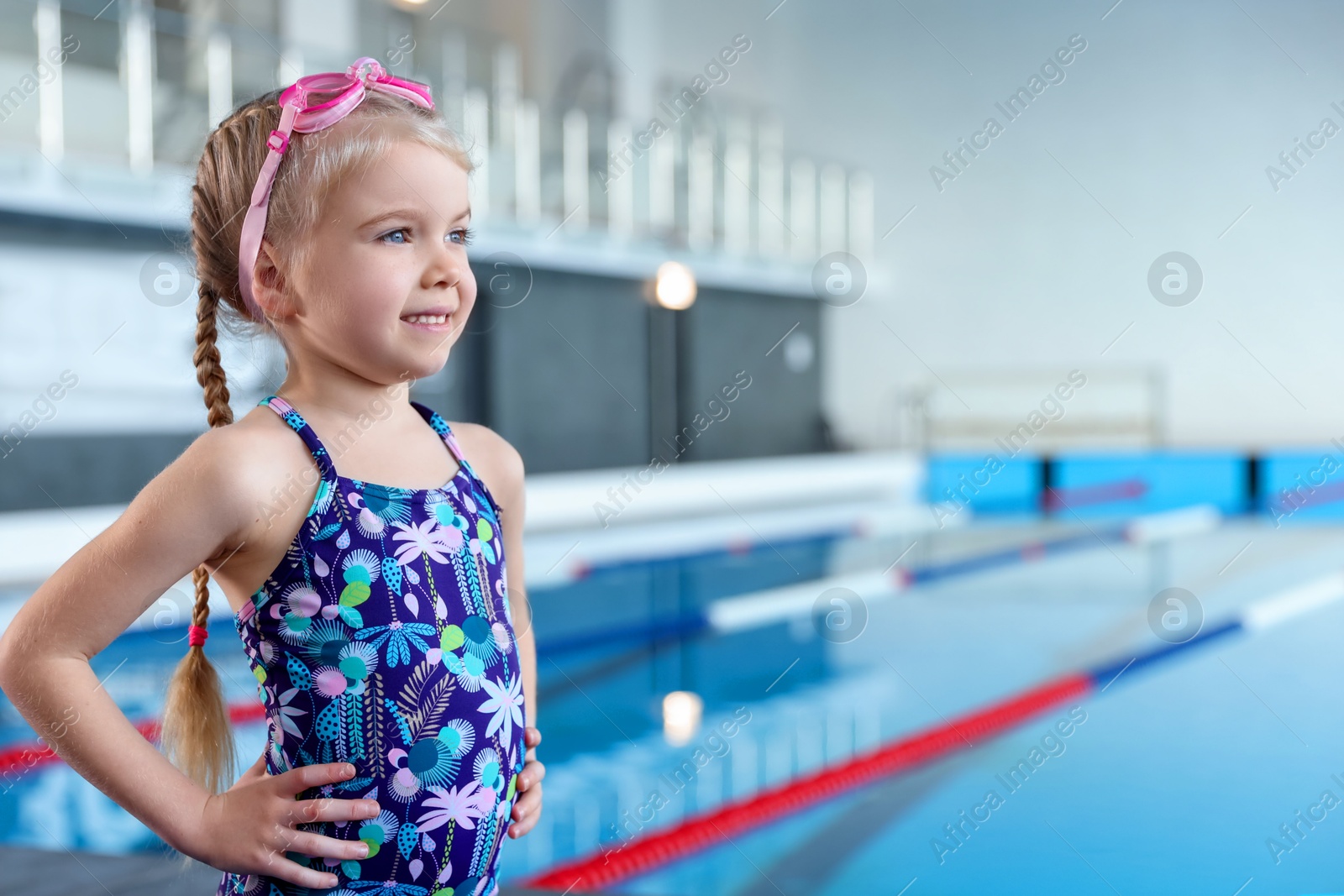 Photo of Little girl with goggles near swimming pool indoors, space for text