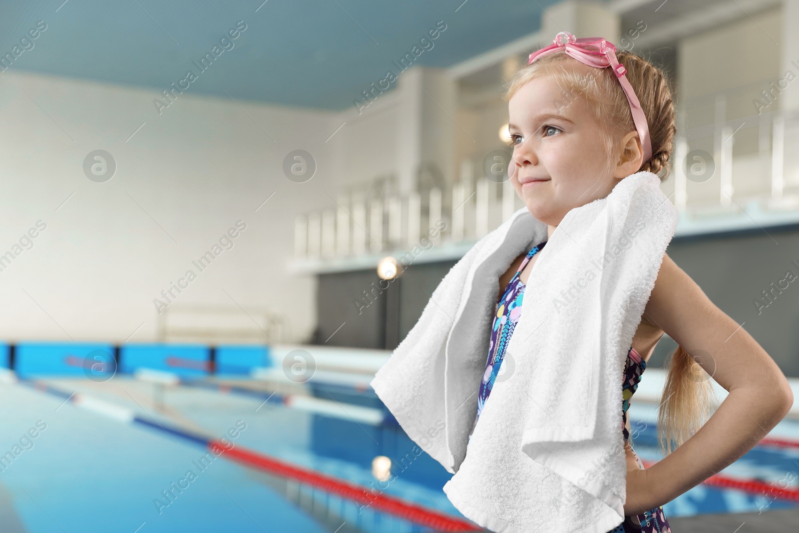 Photo of Little girl with goggles and towel near swimming pool indoors, space for text