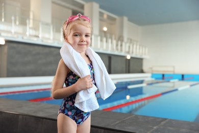 Photo of Little girl with goggles and towel near swimming pool indoors, space for text