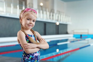 Photo of Little girl with goggles near swimming pool indoors, space for text