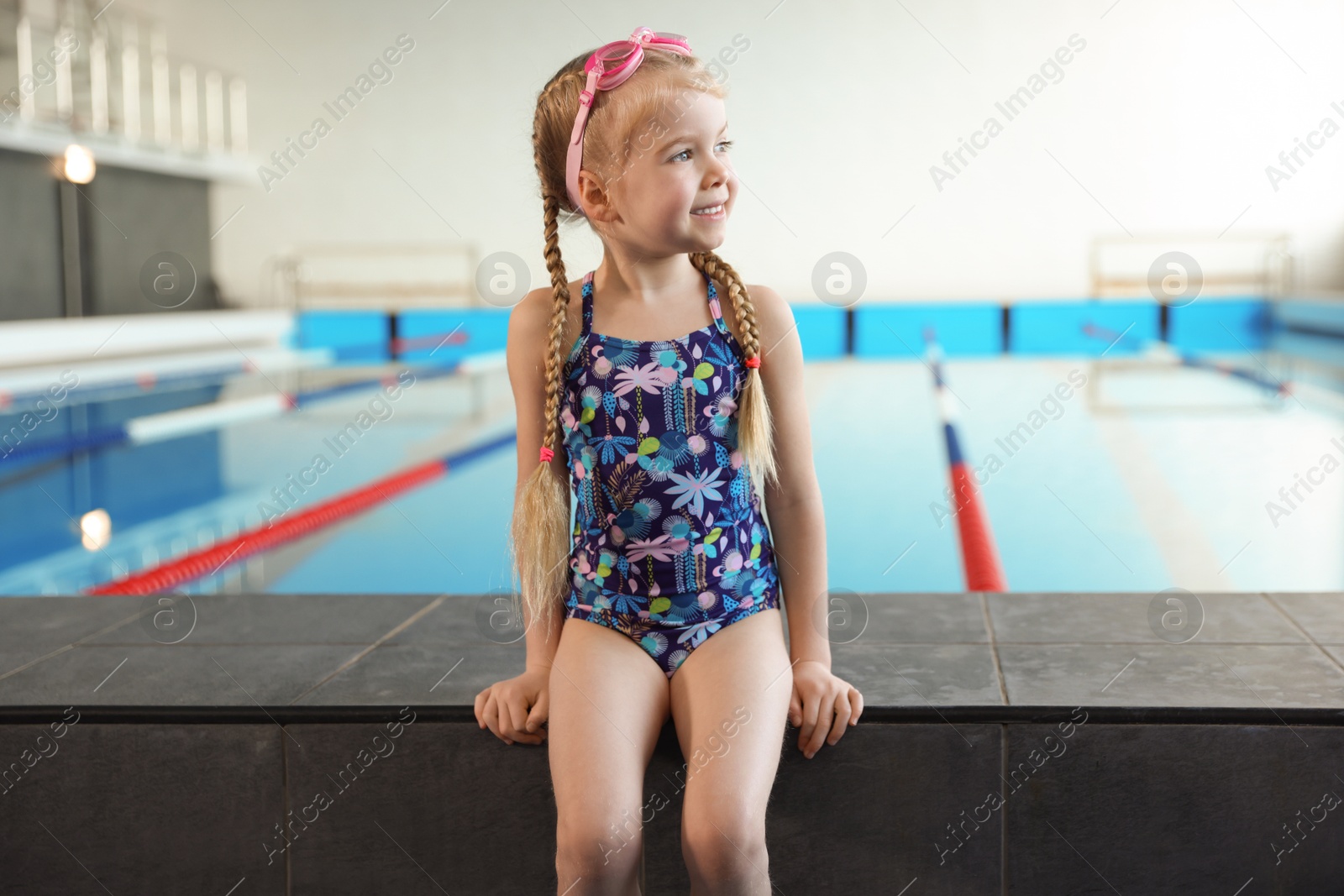 Photo of Little girl with goggles near swimming pool indoors