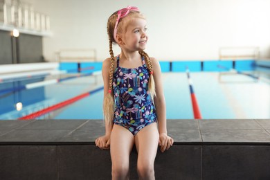 Photo of Little girl with goggles near swimming pool indoors