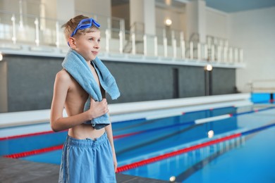 Photo of Boy with goggles and towel near swimming pool indoors, space for text