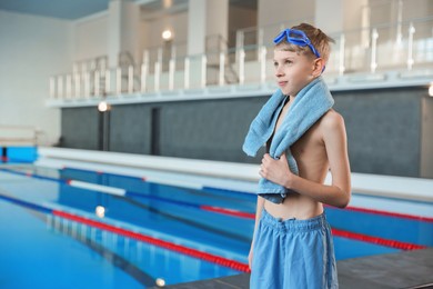 Photo of Boy with goggles and towel near swimming pool indoors, space for text