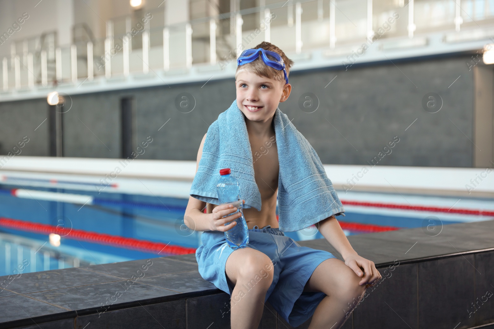 Photo of Boy with goggles, towel and water near swimming pool indoors