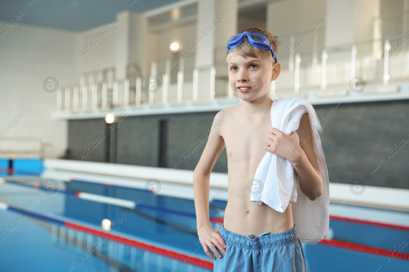 Photo of Boy with goggles and towel near swimming pool indoors, space for text