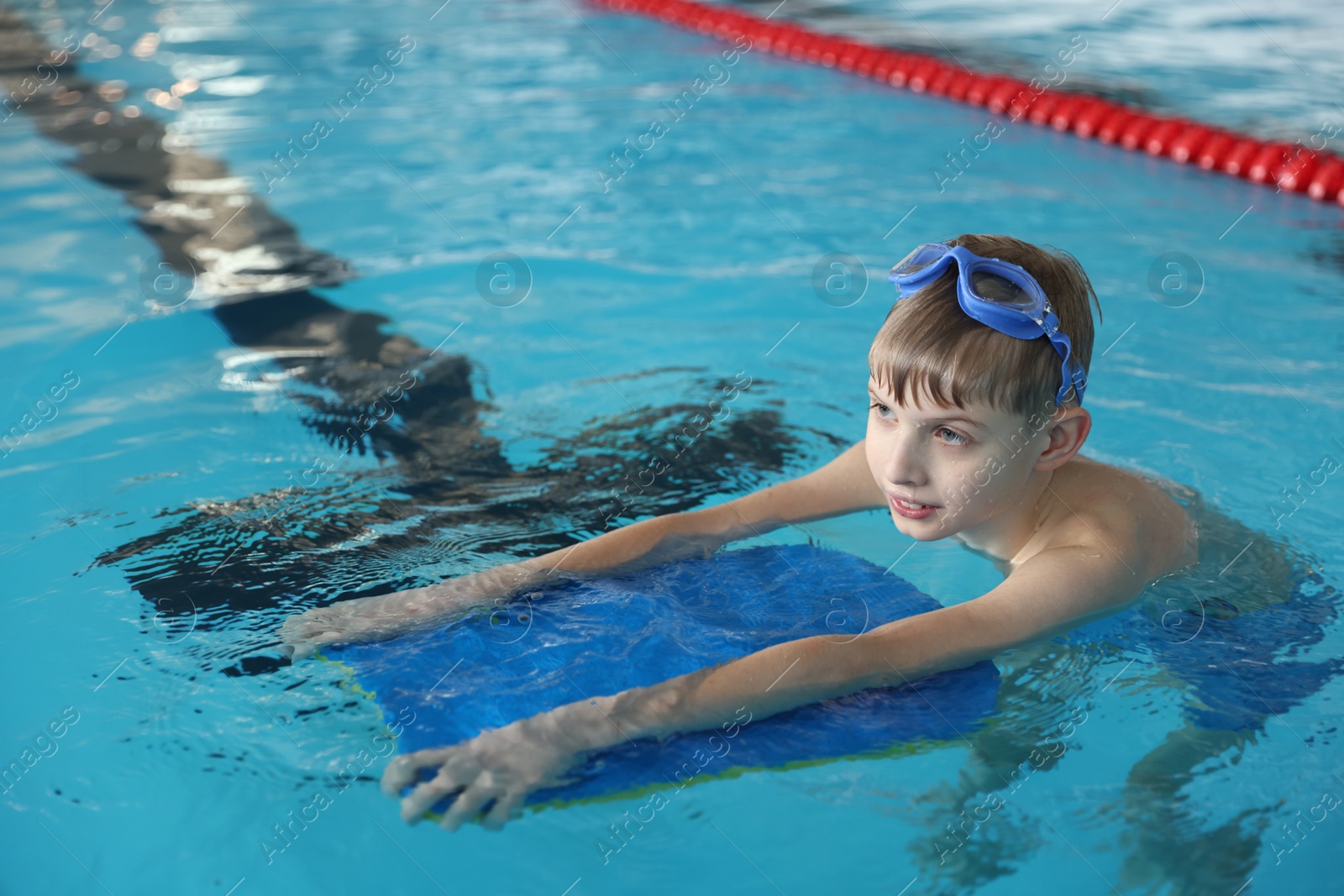 Photo of Boy with goggles and kickboard swimming pool indoors