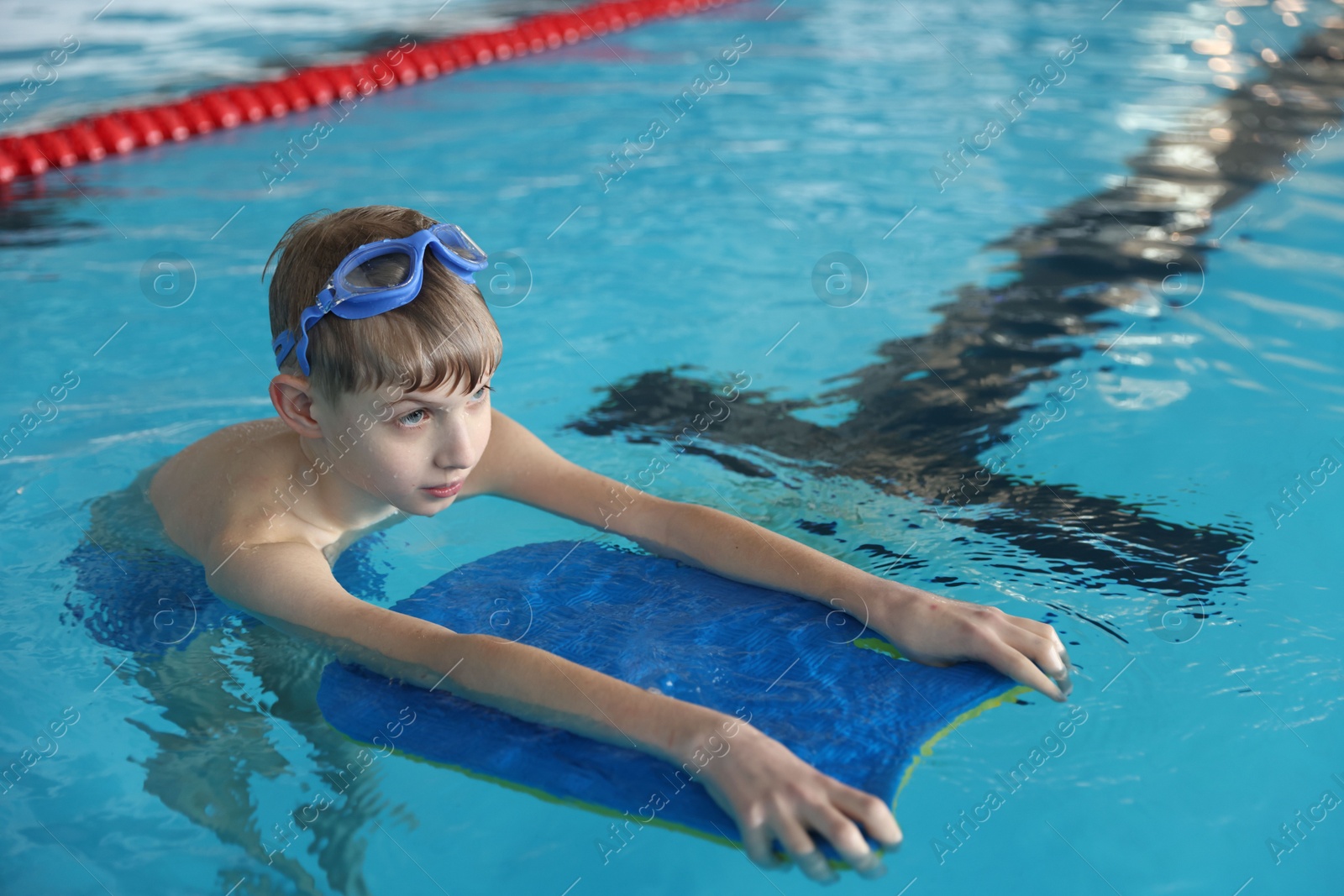 Photo of Boy with goggles and kickboard swimming pool indoors