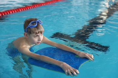 Photo of Boy with goggles and kickboard swimming pool indoors