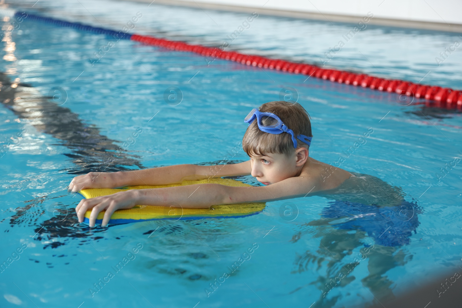 Photo of Boy with goggles and kickboard swimming pool indoors