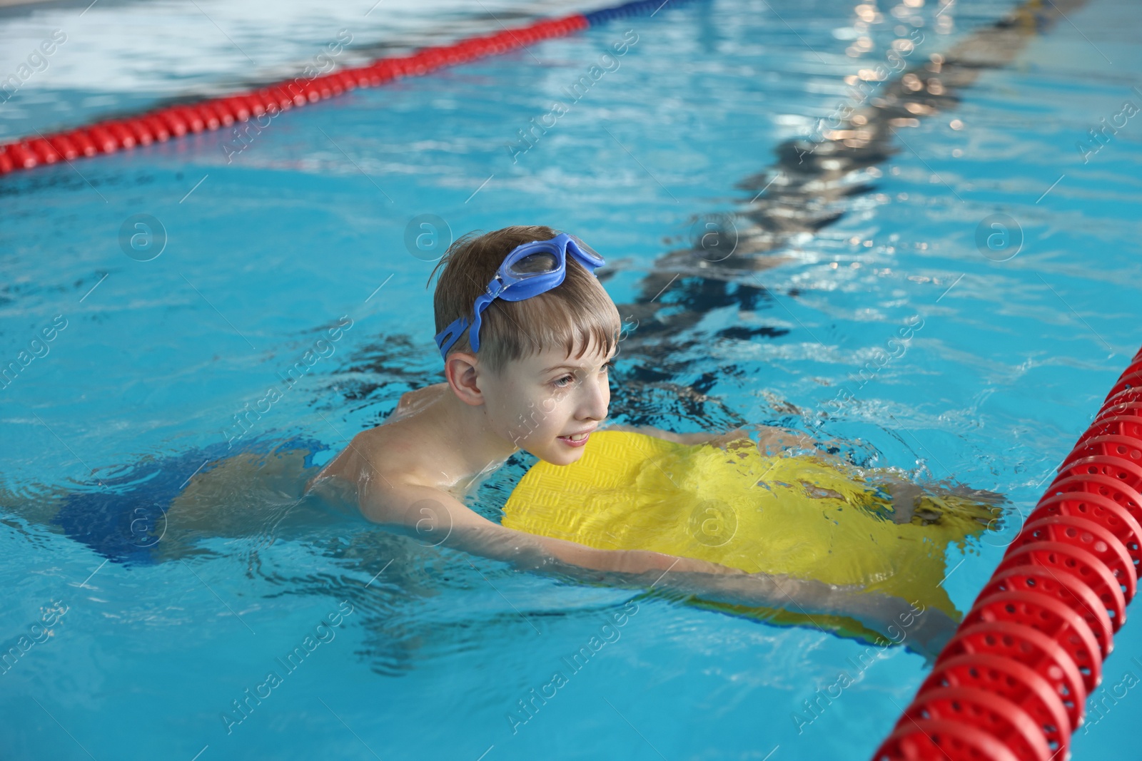 Photo of Boy with goggles and kickboard swimming pool indoors