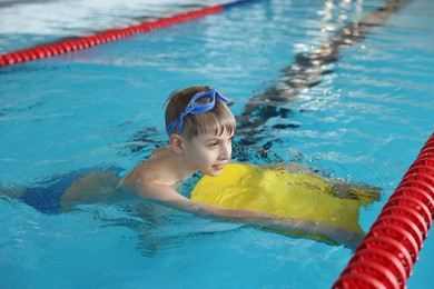 Photo of Boy with goggles and kickboard swimming pool indoors