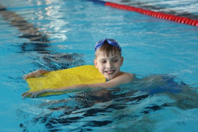 Photo of Boy with goggles and kickboard swimming pool indoors