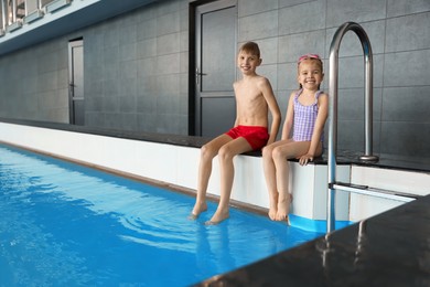 Photo of Children sitting near swimming pool indoors, space for text