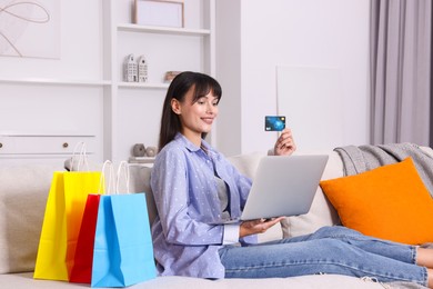 Photo of Internet shopping. Happy woman with credit card, laptop and colorful bags on sofa at home