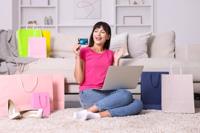 Photo of Internet shopping. Happy woman with credit card, laptop and colorful bags at home