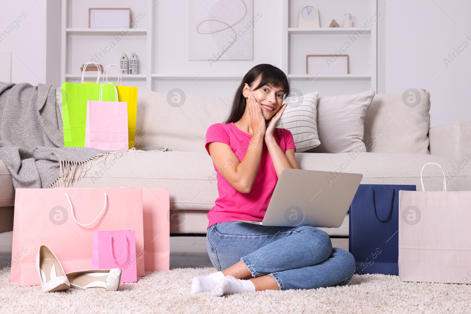 Photo of Internet shopping. Happy woman with laptop and colorful bags at home