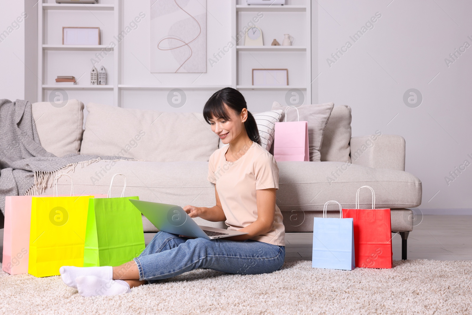 Photo of Internet shopping. Happy woman with laptop and colorful bags at home