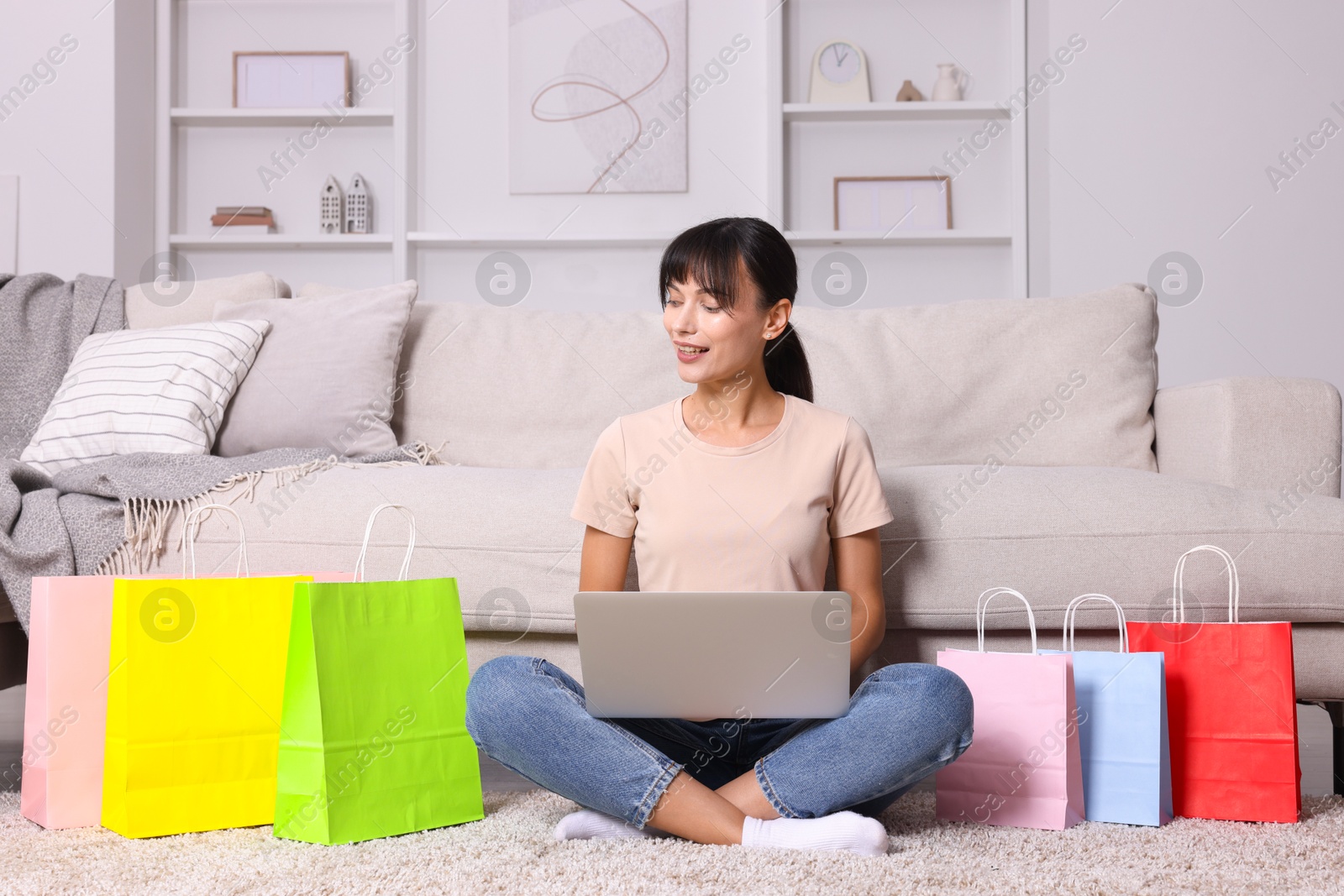 Photo of Internet shopping. Happy woman with laptop and colorful bags at home