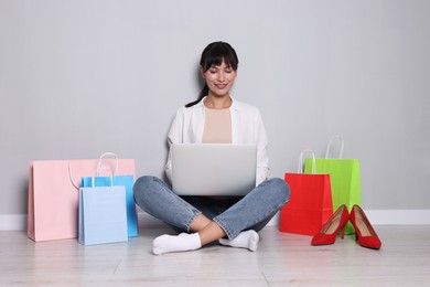 Photo of Internet shopping. Happy woman with laptop and colorful bags sitting near grey wall