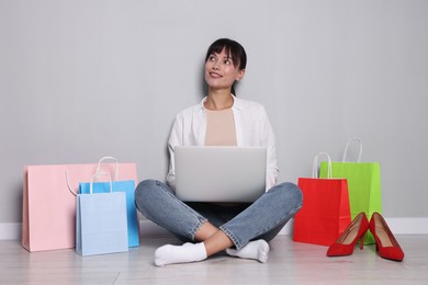 Photo of Internet shopping. Happy woman with laptop and colorful bags sitting near grey wall