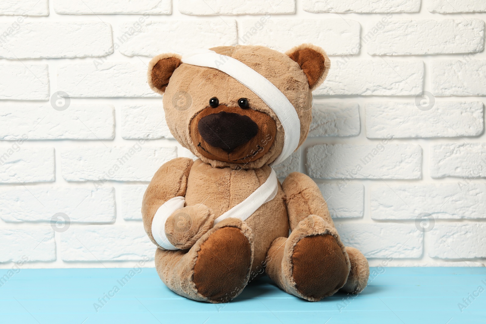 Photo of Teddy bear with bandages on light blue wooden table against white brick wall