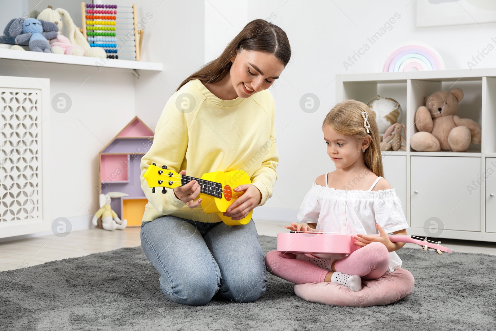 Photo of Young woman teaching little girl to play ukulele at home