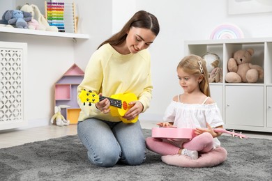 Photo of Young woman teaching little girl to play ukulele at home