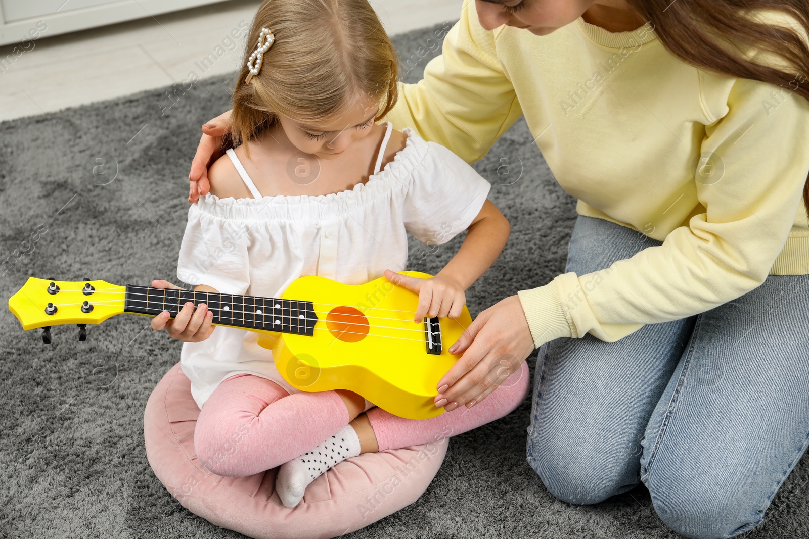 Photo of Young woman teaching little girl to play ukulele at home