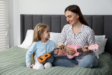 Photo of Young woman teaching little girl to play ukulele at home