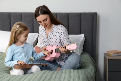 Photo of Young woman teaching little girl to play ukulele at home