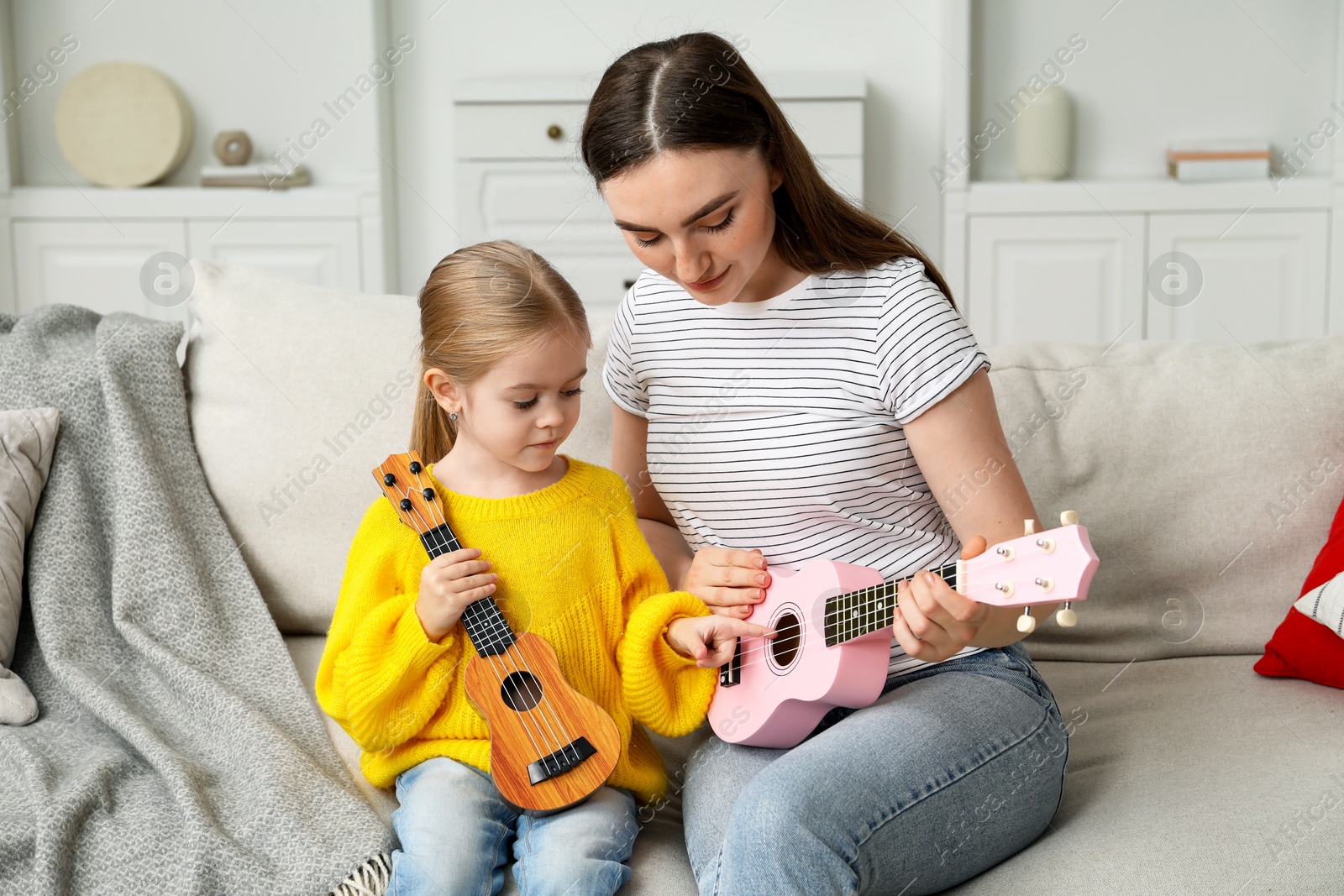 Photo of Young woman teaching little girl to play ukulele at home