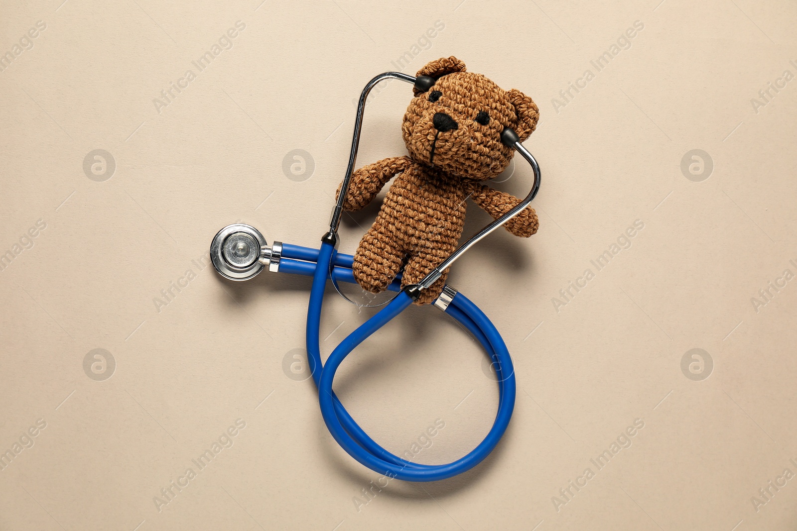 Photo of Pediatrics concept. Toy bear with stethoscope on beige background, top view