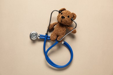 Photo of Pediatrics concept. Toy bear with stethoscope on beige background, top view