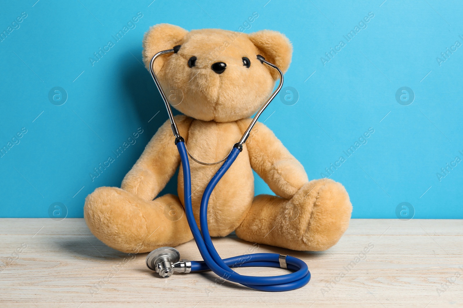 Photo of Pediatrics concept. Teddy bear with stethoscope on wooden table against light blue background