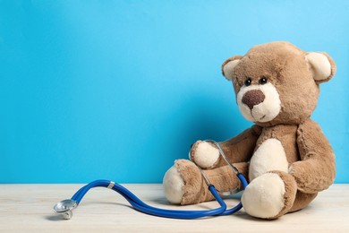 Photo of Pediatrics concept. Teddy bear with stethoscope on wooden table against light blue background, space for text