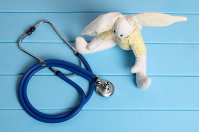 Photo of Pediatrics concept. Toy bunny and stethoscope on light blue wooden table, above view