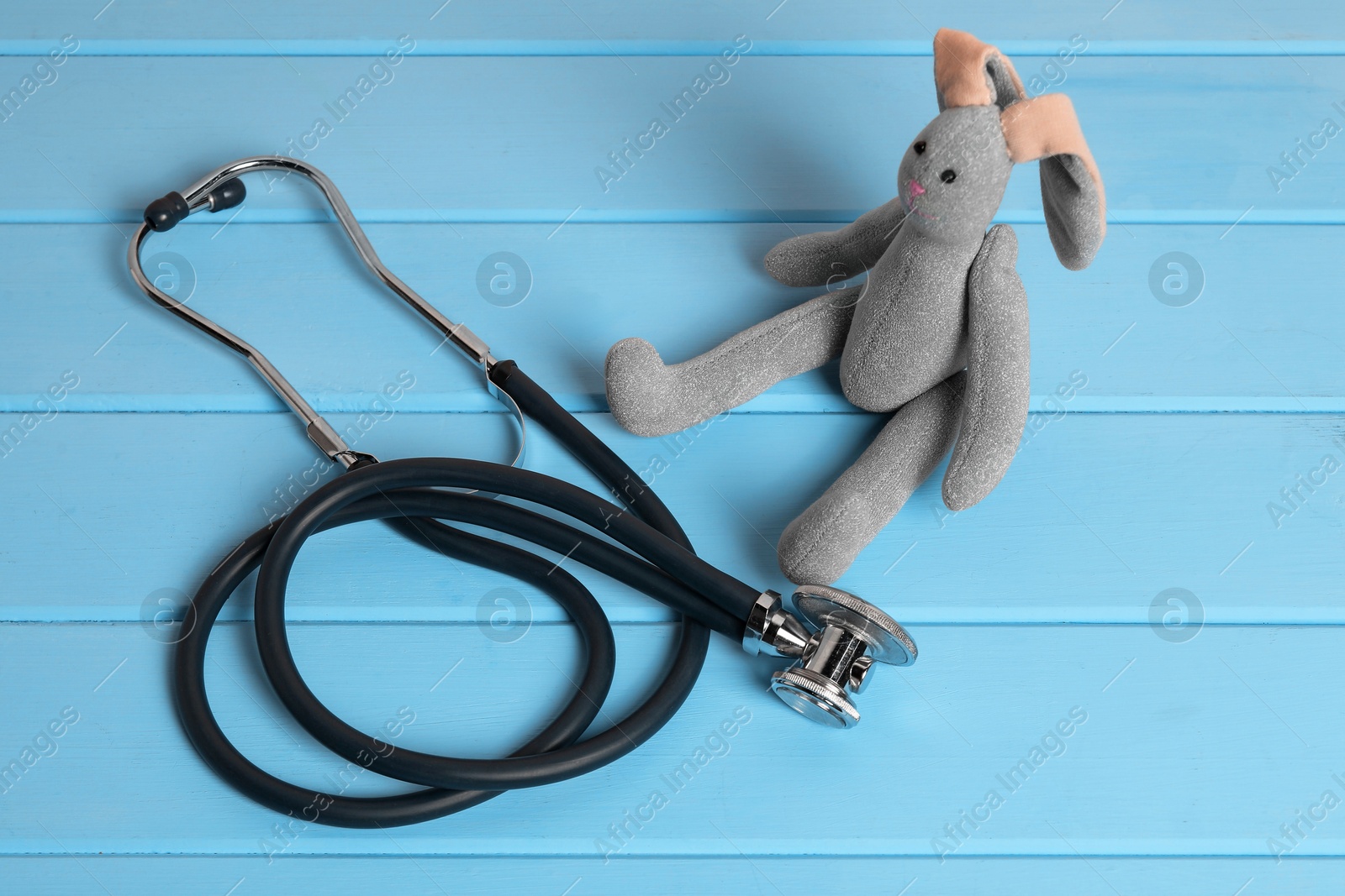 Photo of Pediatrics concept. Toy bunny and stethoscope on light blue wooden table