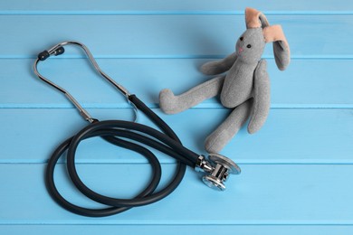 Photo of Pediatrics concept. Toy bunny and stethoscope on light blue wooden table