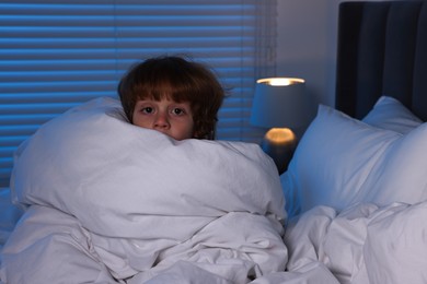 Scared boy wrapped in duvet on bed at night