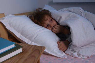 Scared boy under duvet in bed at night