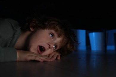 Fearful boy hiding under bed at night