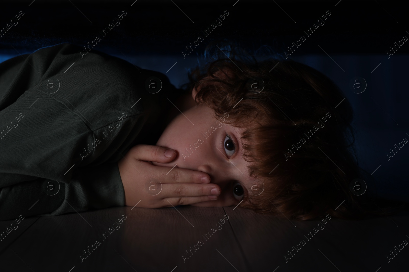 Photo of Fearful boy hiding under bed at night