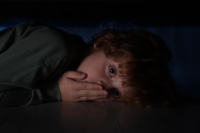 Fearful boy hiding under bed at night