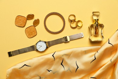 Photo of Many stylish jewelry, perfume and accessories on pale yellow background, flat lay