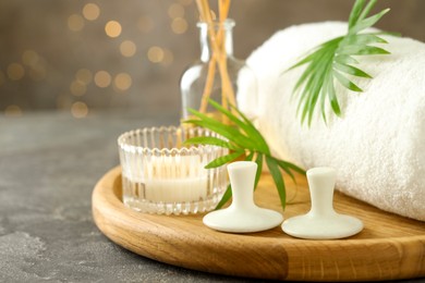 Photo of Spa stones, burning candle, towel and green leaves on grey table, closeup