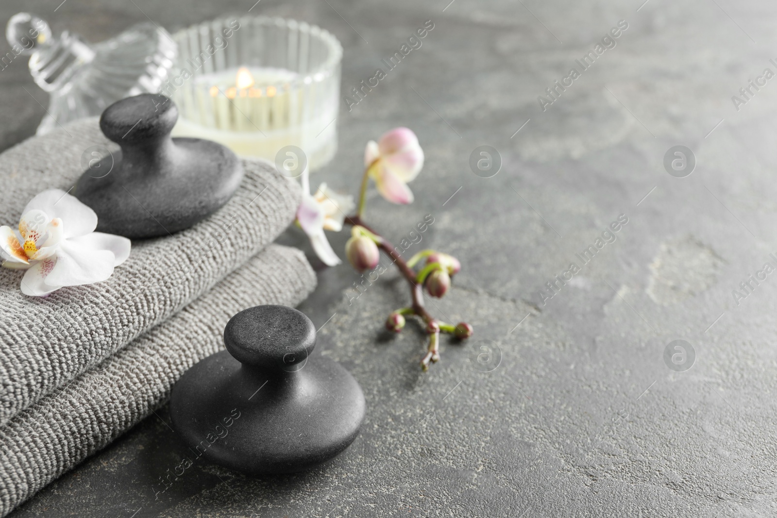 Photo of Spa stones, towels, orchid flowers and candle on grey table, closeup. Space for text