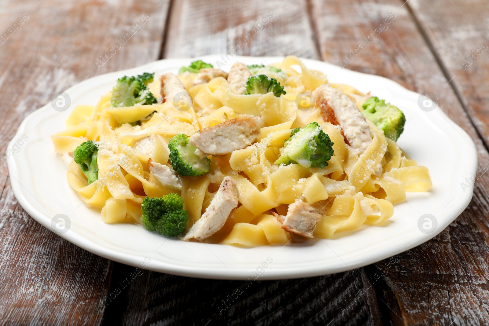 Photo of Delicious pasta Alfredo with chicken, cheese and broccoli on wooden table, closeup