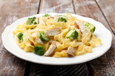 Photo of Delicious pasta Alfredo with chicken, cheese and broccoli on wooden table, closeup