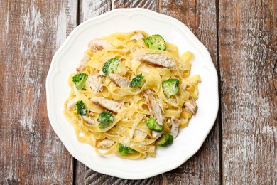 Photo of Delicious pasta Alfredo with chicken, cheese and broccoli on wooden table, top view